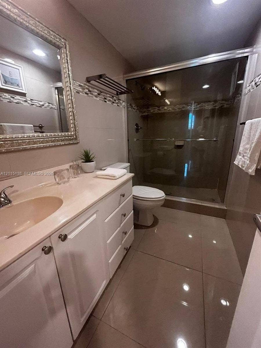 19380 Collins Avenue, #1602, Sunny Isles Beach, FL 33160 Bathroom featuring white cabinetry, integrated countertop with oval sink, glass-enclosed shower, mosaic tile accent border, and large-format tile flooring