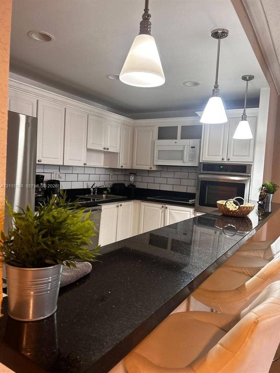 19380 Collins Avenue, #1602, Sunny Isles Beach, FL 33160 Kitchen featuring white cabinetry, dark stone countertops, a subway tile backsplash, built-in stainless steel appliances, and three glass pendant lights