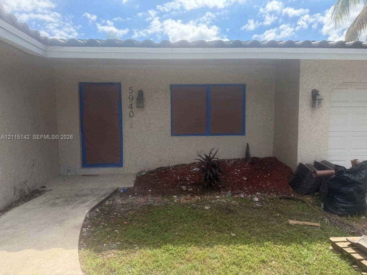 5940 SW 18th Street, Plantation, FL 33317 Stucco exterior featuring a tile roof, concrete walkway, and wall-mounted exterior lighting