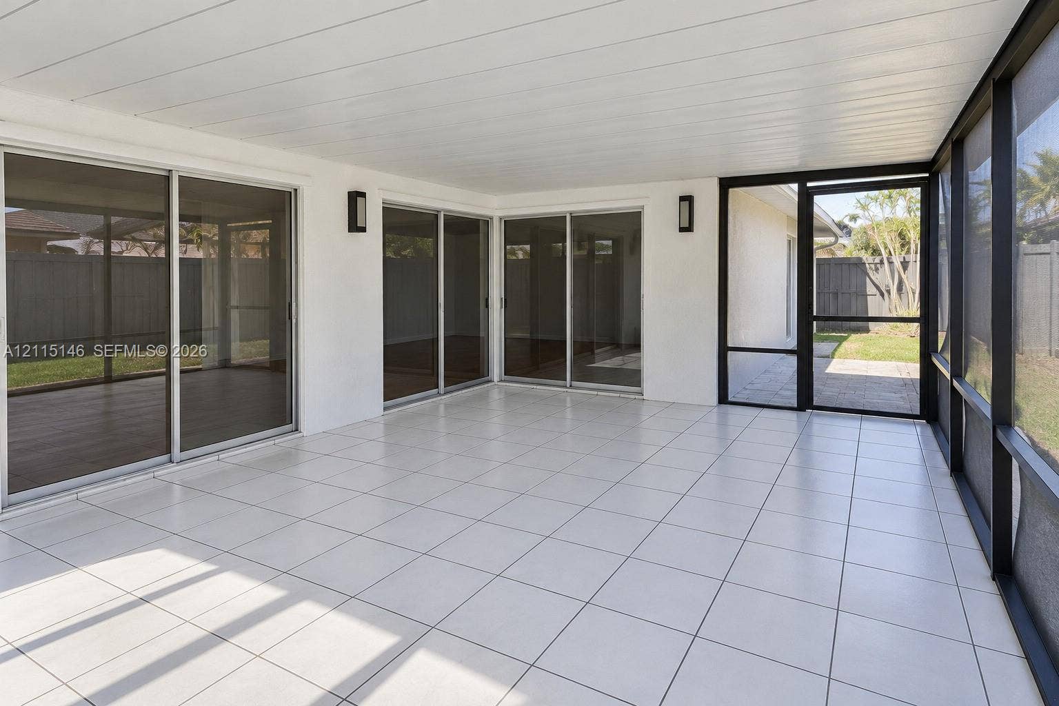 Screened-in patio featuring tile flooring, a paneled ceiling, dual wall-mounted light fixtures, and multiple sliding glass doors
