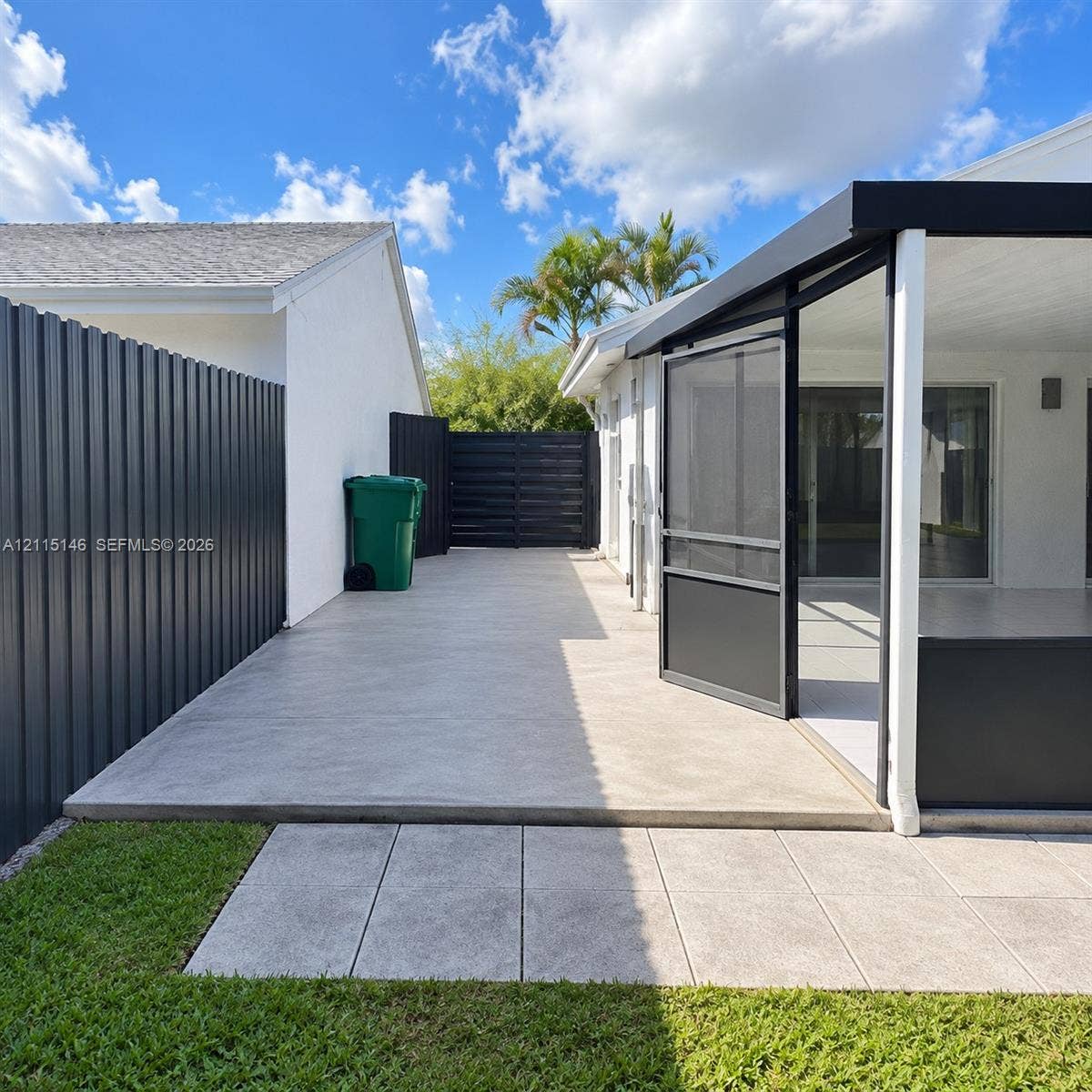 Concrete patio area featuring a screened-in enclosure, metal perimeter fencing, and paver accents