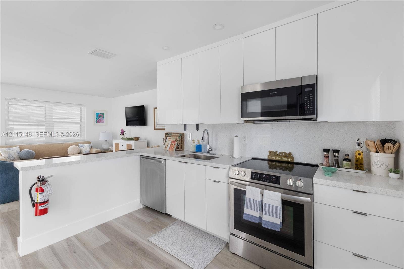 Kitchen featuring white flat-panel cabinetry, light-toned stone countertops, stainless steel appliances, and wood-finish flooring
