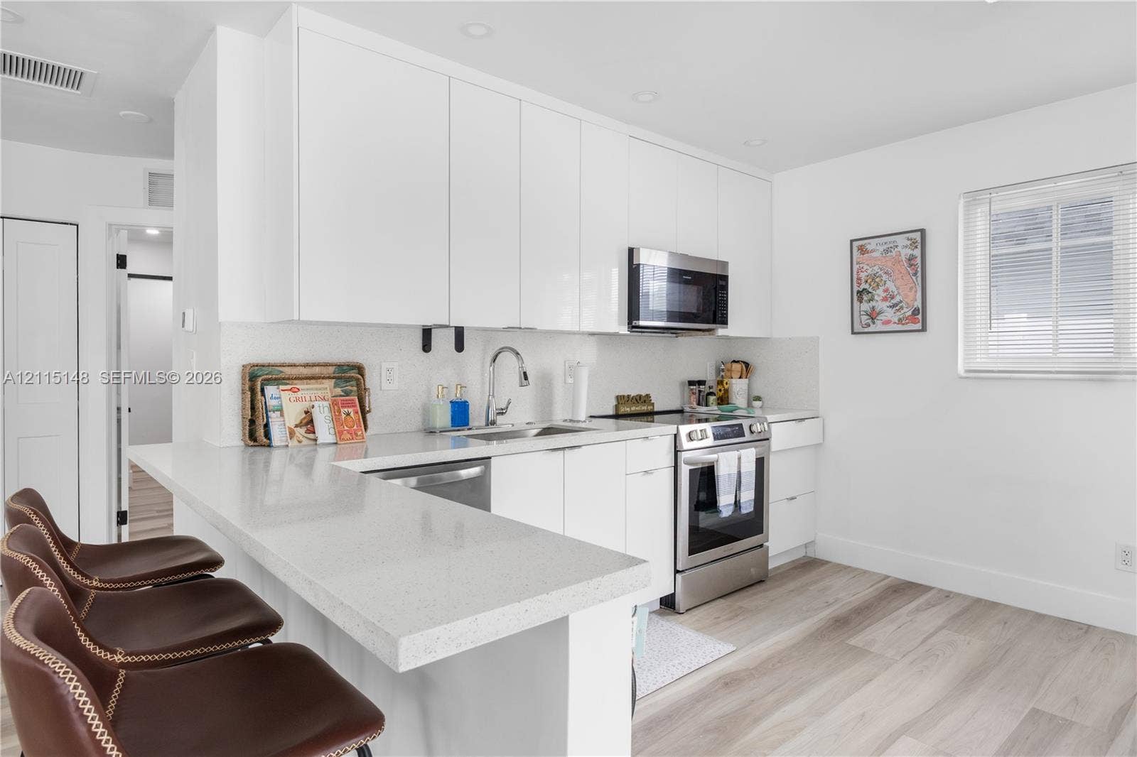 Kitchen featuring high-gloss white cabinetry, quartz countertops, a peninsula with bar seating, stainless steel appliances, and wood-finish flooring