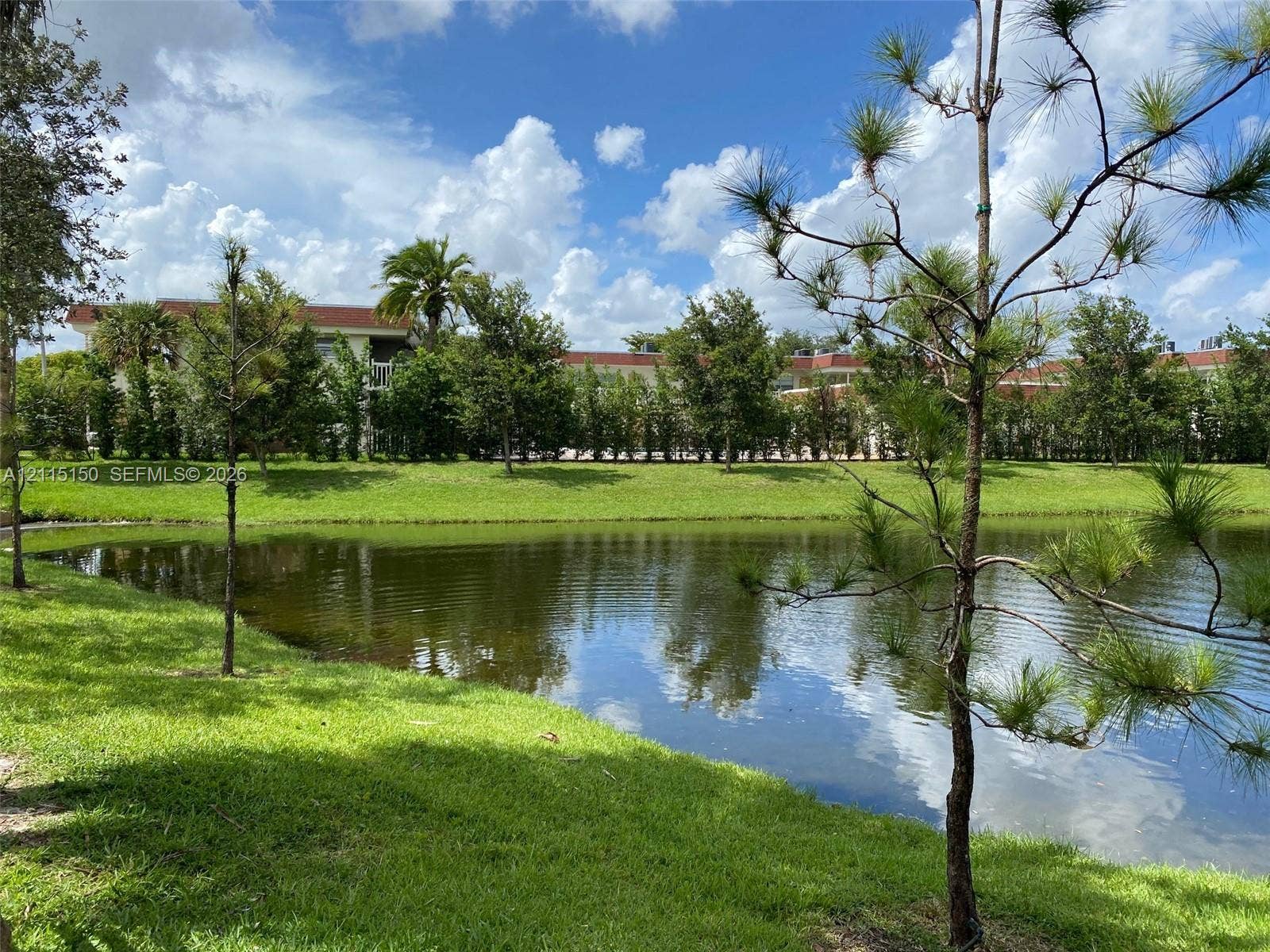 6992 SW 39th Street, #I201, Davie, Davie, FL 33314 Waterfront property featuring a pond, manicured lawn, mature trees, and landscaping