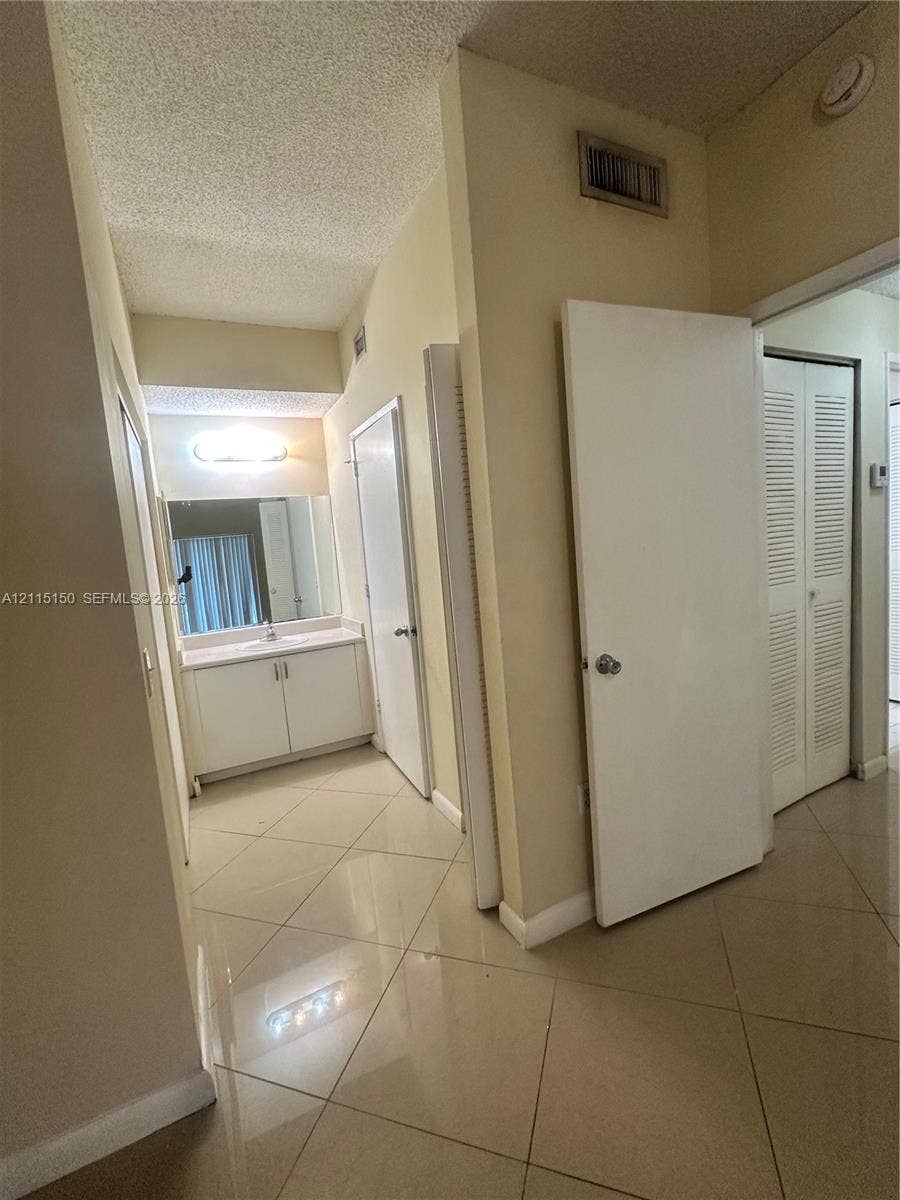 6992 SW 39th Street, #I201, Davie, Davie, FL 33314 Large-format tile flooring, built-in vanity with integrated basin, expansive wall mirror, and louvered closet doors