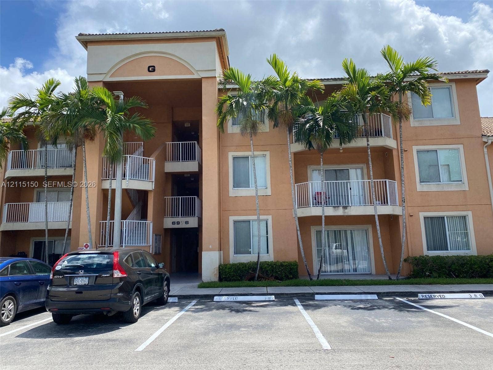 6992 SW 39th Street, #I201, Davie, Davie, FL 33314 Multi-story exterior featuring a stucco facade, arched entryway, private balconies with metal railings, and mature palm trees