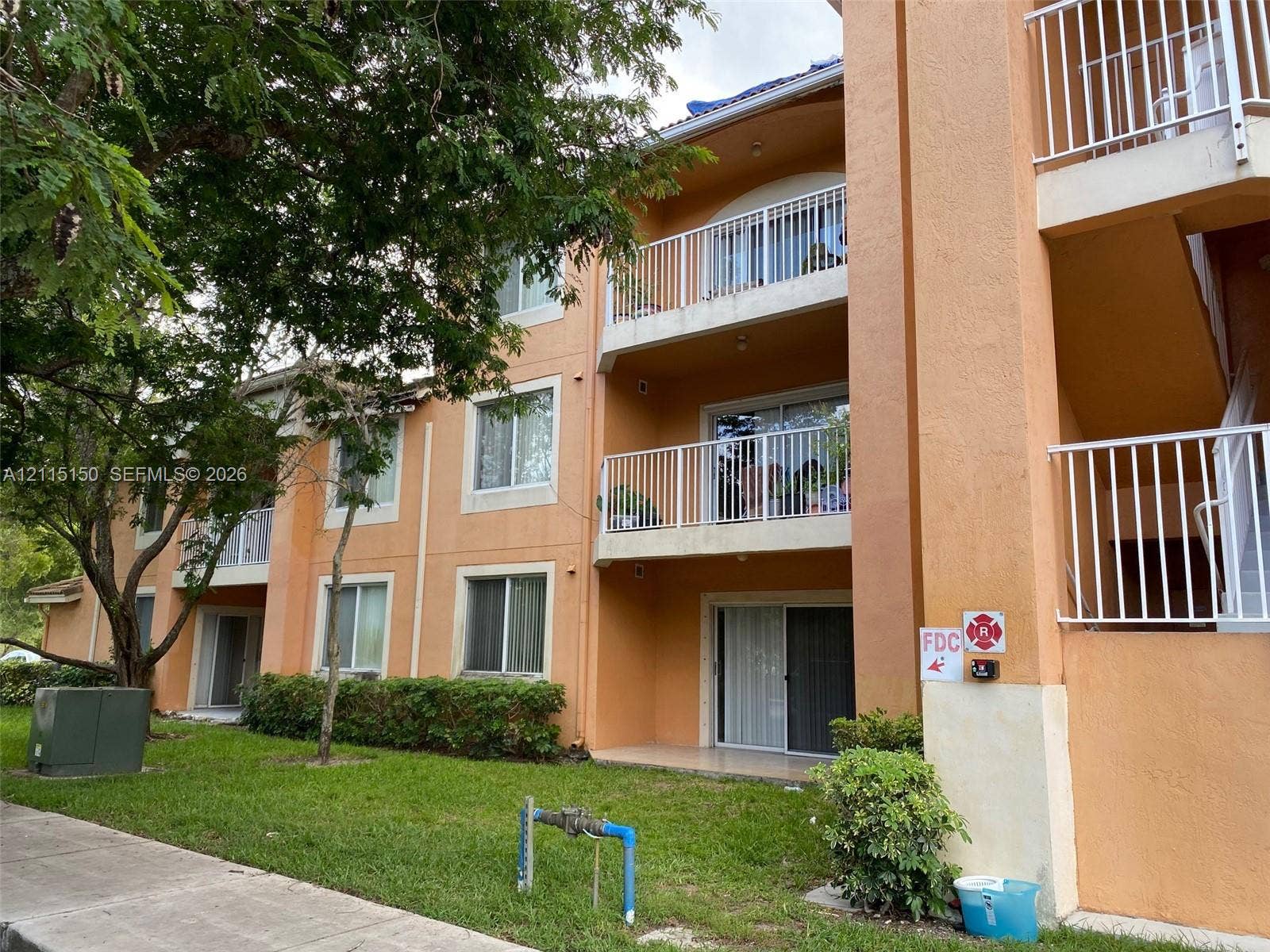 6992 SW 39th Street, #I201, Davie, Davie, FL 33314 Multi-level exterior featuring stucco siding, white metal railings, sliding glass balcony doors, and ground-level patios