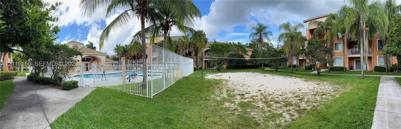 6992 SW 39th Street, #I201, Davie, Davie, FL 33314 Outdoor recreation area featuring a sand volleyball court, fenced swimming pool, concrete walkways, and mature palm trees