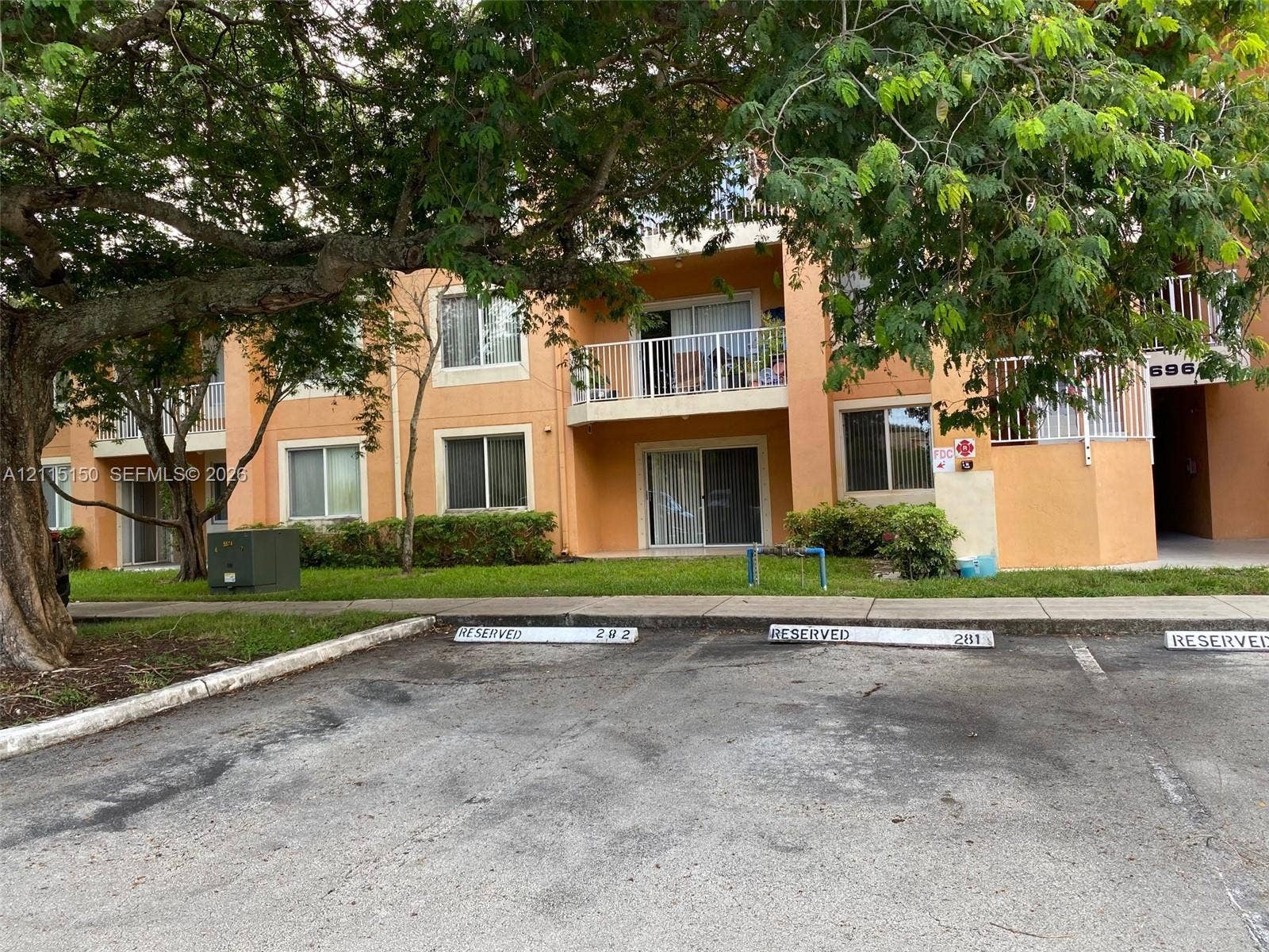 6992 SW 39th Street, #I201, Davie, Davie, FL 33314 Multi-story residential building featuring a stucco exterior, private balconies with white railings, sliding glass doors, and designated parking spaces