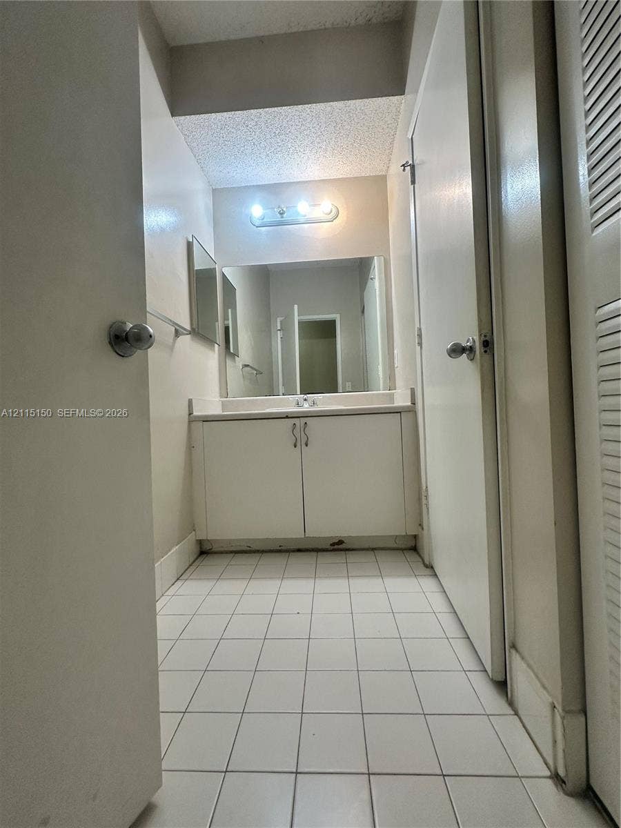 6992 SW 39th Street, #I201, Davie, Davie, FL 33314 Bathroom vanity featuring a white cabinet base, integrated countertop, and mounted light fixture, complemented by tiled flooring