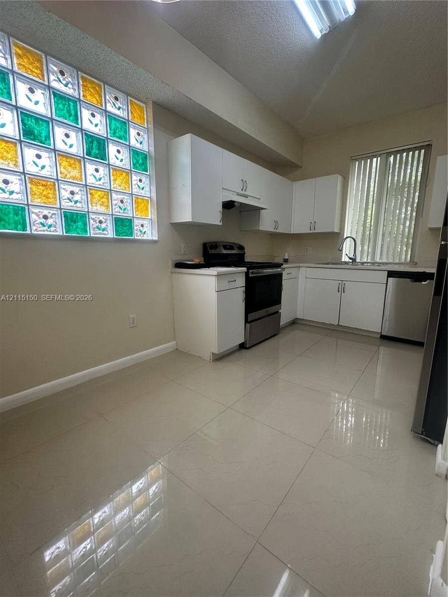 6992 SW 39th Street, #I201, Davie, Davie, FL 33314 Kitchen featuring white cabinetry, large-format tile flooring, stainless steel appliances, and a glass block window with multicolor accents