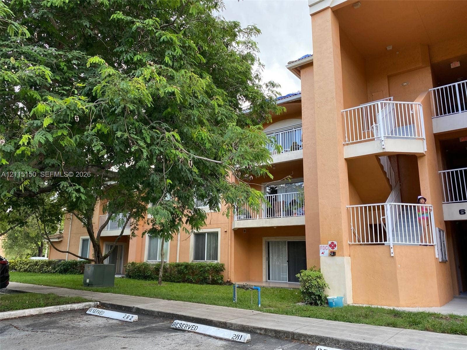 6992 SW 39th Street, #I201, Davie, Davie, FL 33314 Multi-story exterior featuring stucco siding, white metal railings, sliding glass balcony doors, and assigned parking spaces