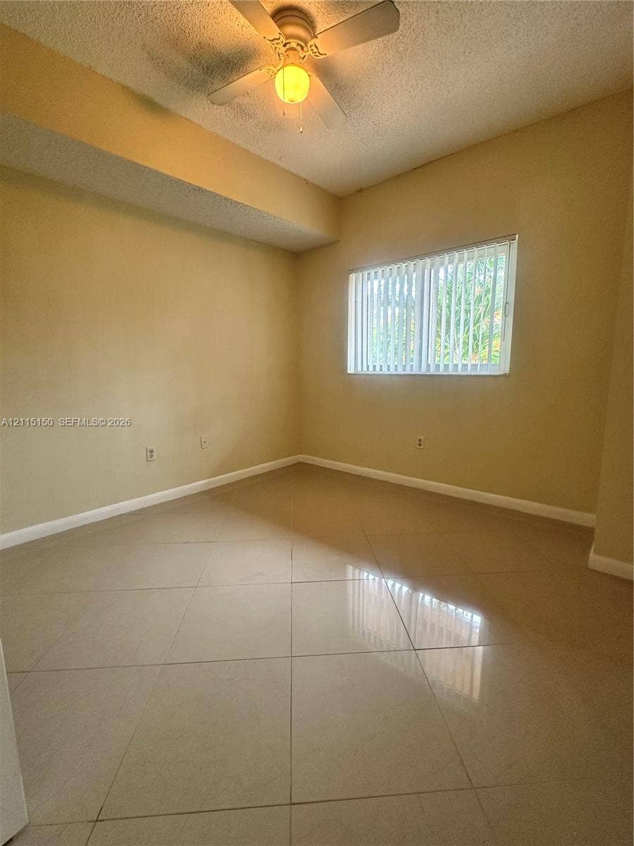 6992 SW 39th Street, #I201, Davie, Davie, FL 33314 Room interior featuring large-format tile flooring, textured ceiling, ceiling fan with integrated light fixture, and horizontal window blinds