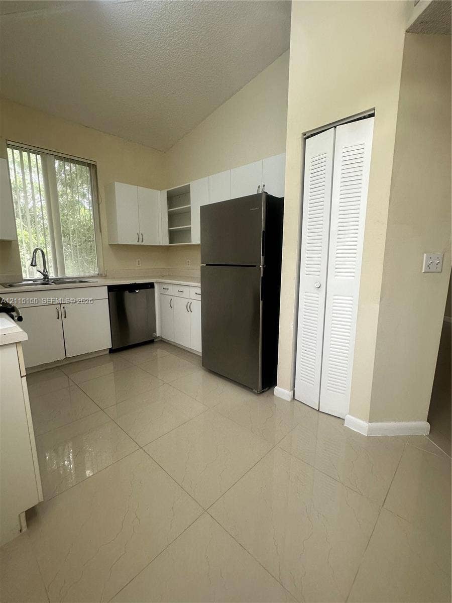 6992 SW 39th Street, #I201, Davie, Davie, FL 33314 Kitchen featuring white cabinetry, stainless steel appliances, tile flooring, louvered closet doors, and a high ceiling