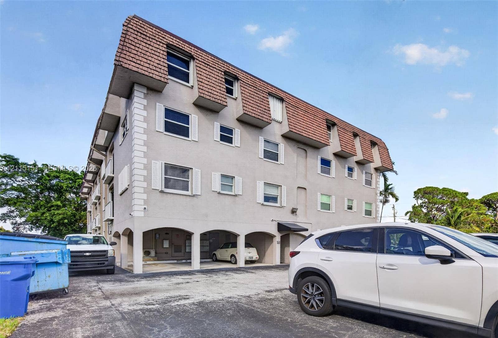 5951 NE 14th Lane, #408N, Fort Lauderdale, FL 33334 Multi-story exterior featuring a mansard roof, stucco facade, decorative window shutters, and covered ground-level parking
