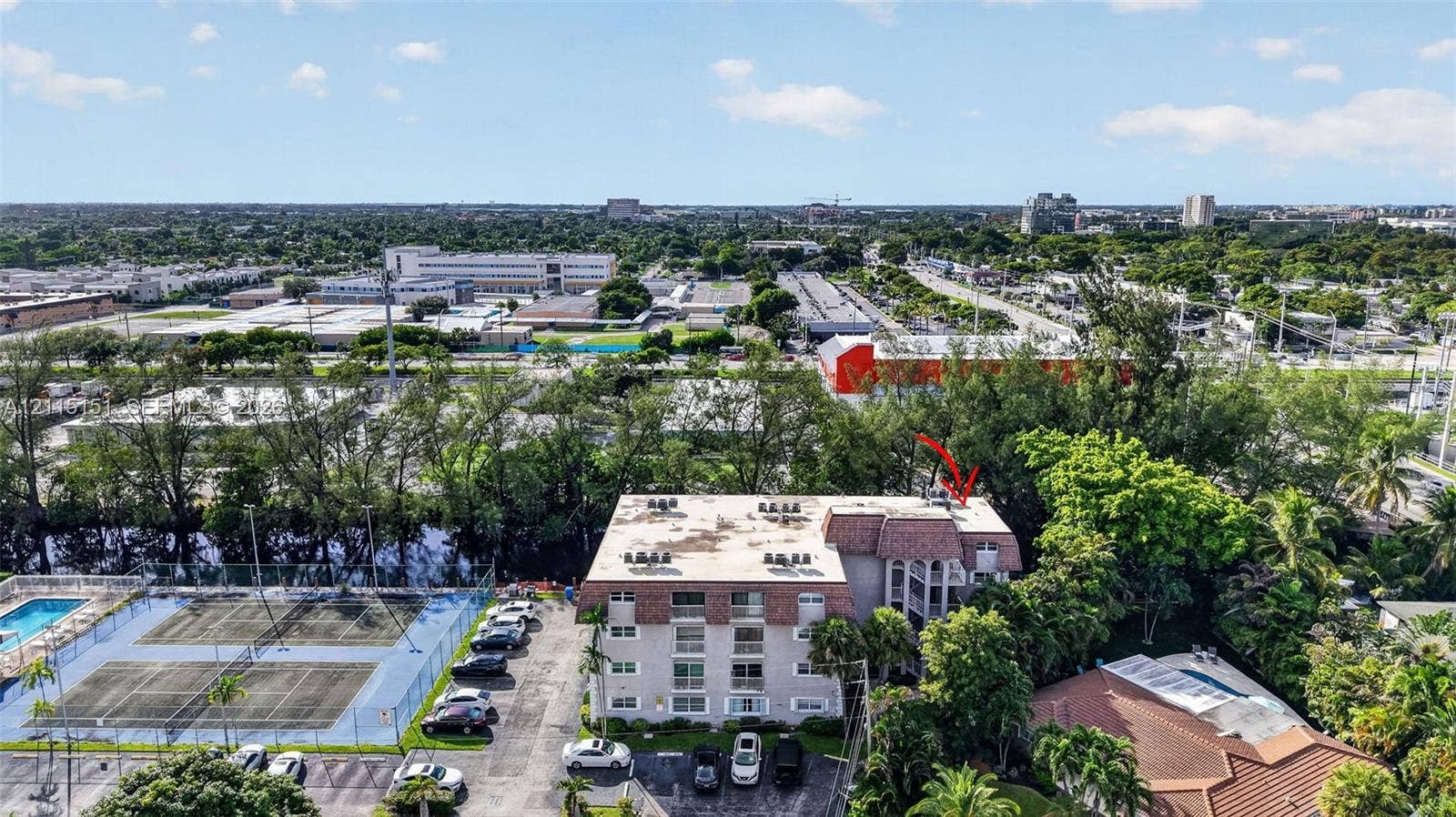 5951 NE 14th Lane, #408N, Fort Lauderdale, FL 33334 Aerial perspective of a multi-story residential building featuring a mansard roof, balconies, surface parking, and a fenced tennis court