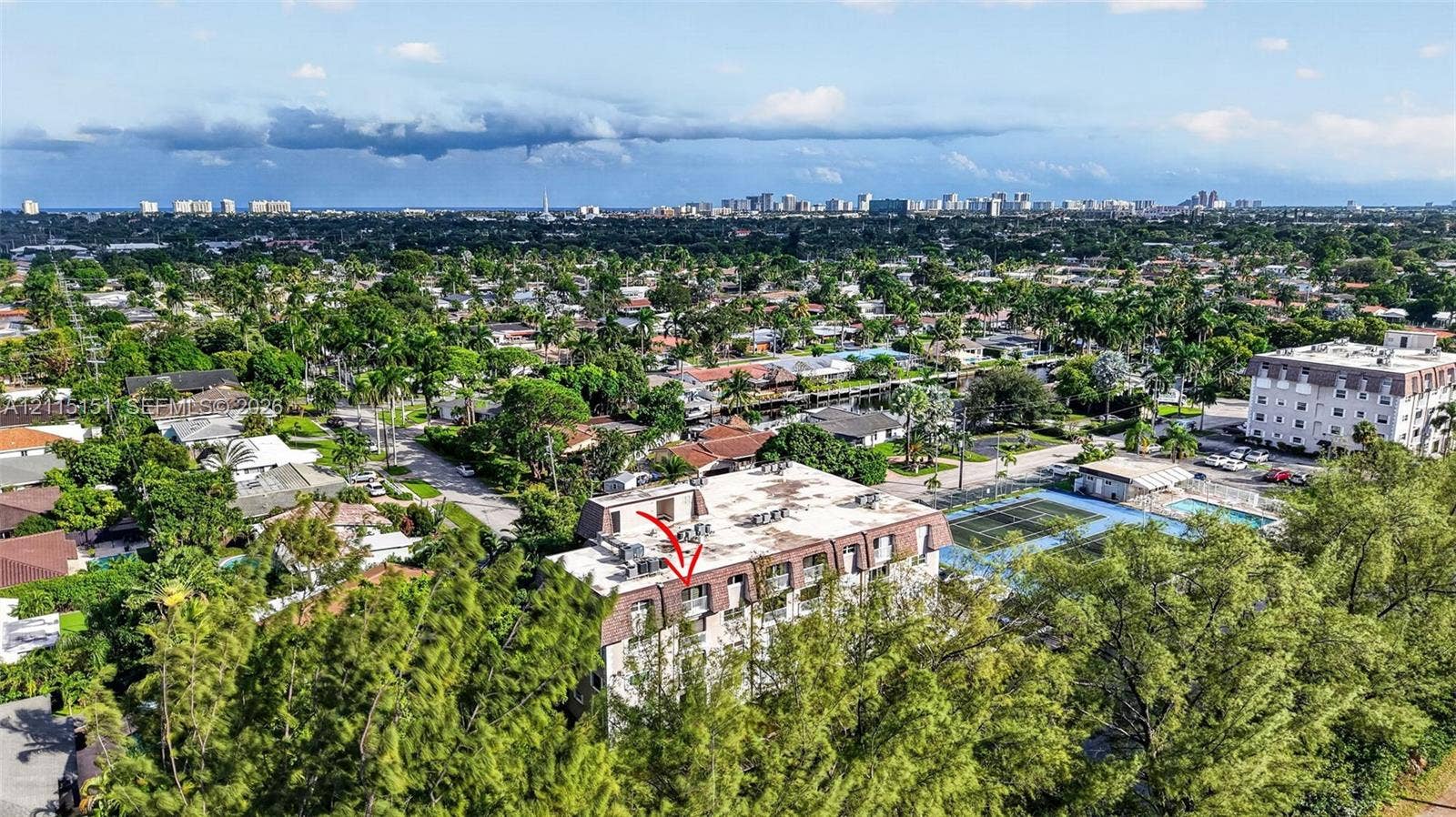 5951 NE 14th Lane, #408N, Fort Lauderdale, FL 33334 Aerial perspective of a multi-story residential building featuring a mansard roof, exterior balconies, and an on-site tennis court