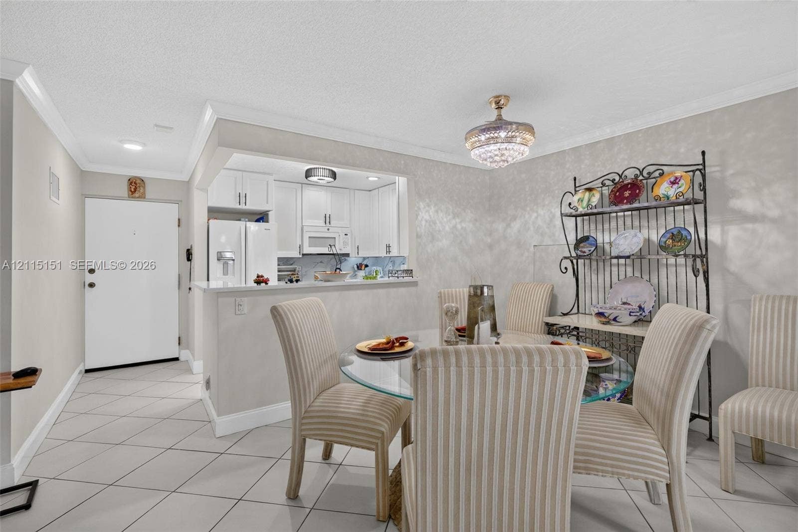 5951 NE 14th Lane, #408N, Fort Lauderdale, FL 33334 Dining area featuring crown molding, a crystal-style chandelier, and ceramic tile flooring, with a pass-through opening to a kitchen equipped with white cabinetry