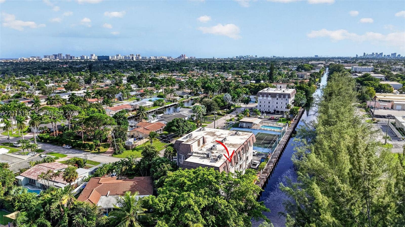 5951 NE 14th Lane, #408N, Fort Lauderdale, FL 33334 Aerial perspective featuring a multi-story residential building with water frontage, a private swimming pool, and dedicated tennis courts