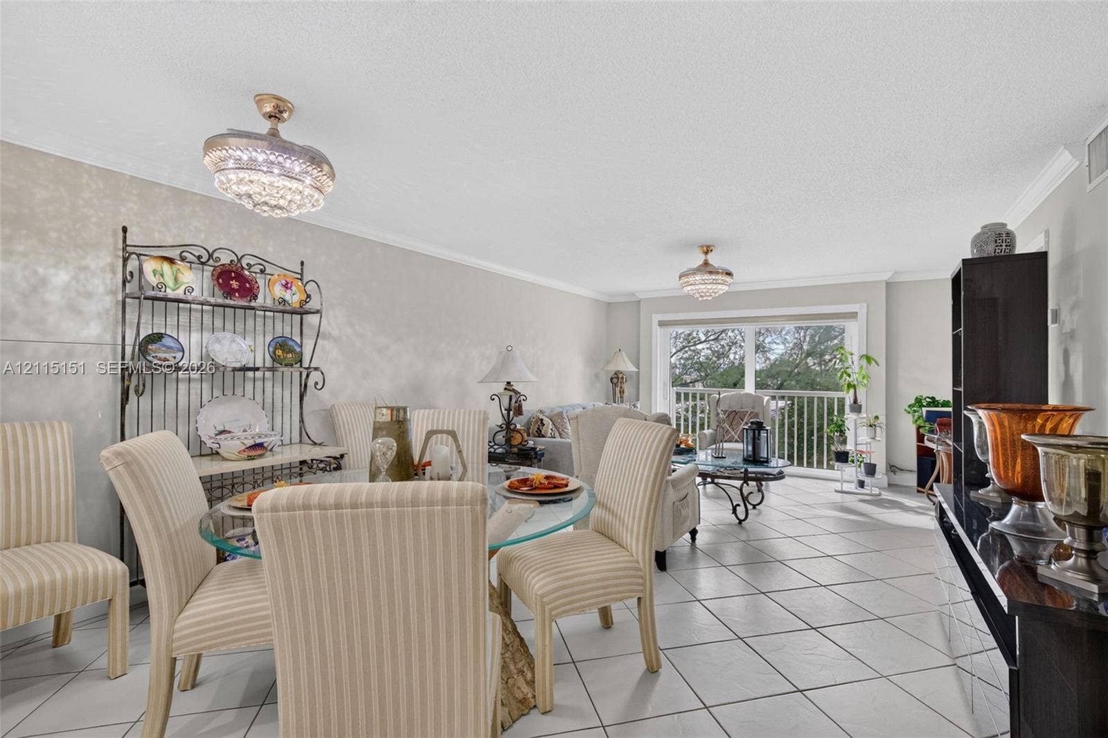 5951 NE 14th Lane, #408N, Fort Lauderdale, FL 33334 Living area featuring large format ceramic tile flooring, twin crystal-accented flush mount chandeliers, crown molding, and sliding glass doors with access to an exterior balcony
