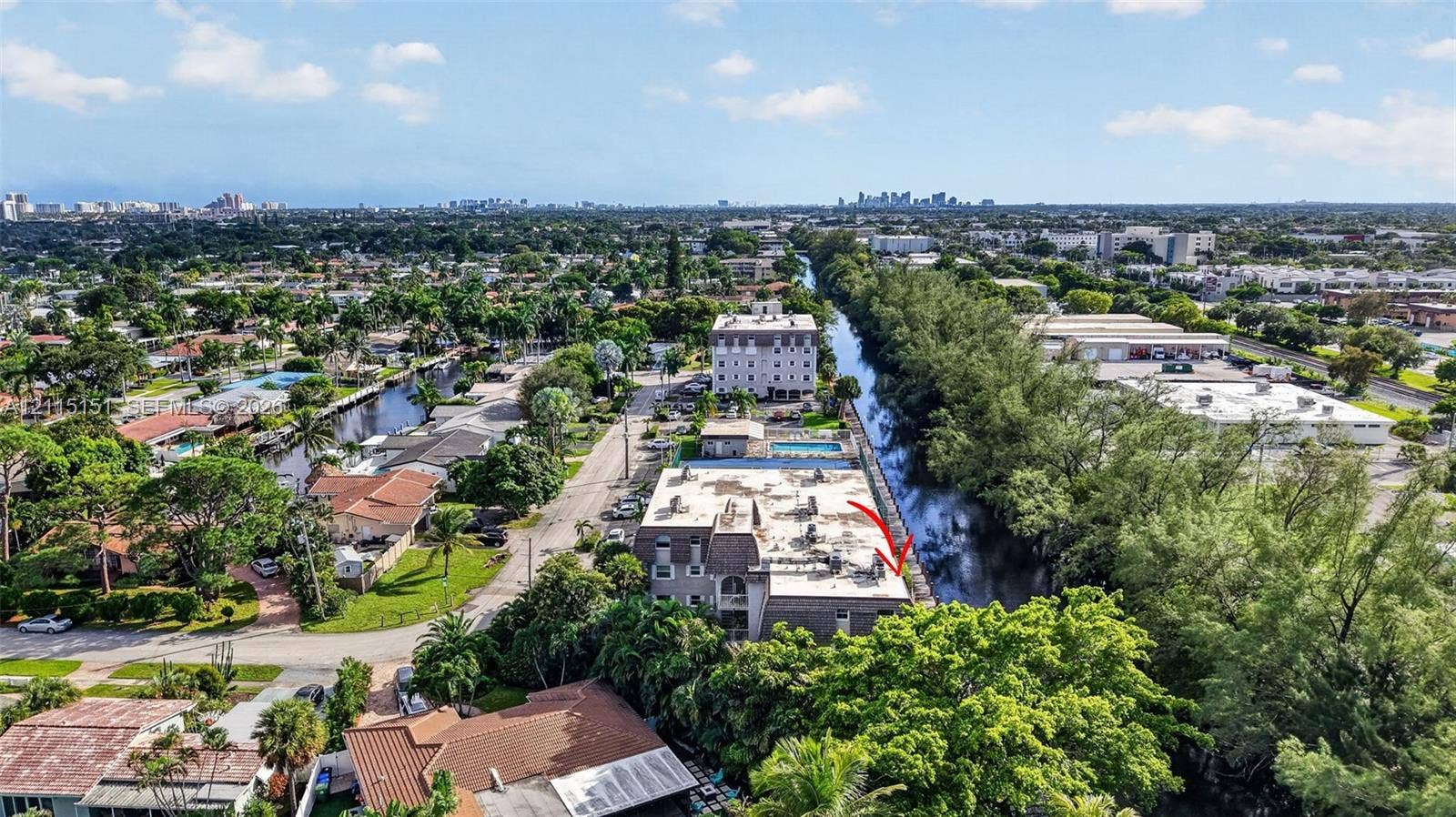 5951 NE 14th Lane, #408N, Fort Lauderdale, FL 33334 Aerial perspective of a multi-story building situated along a canal, featuring a flat roofline and dense surrounding mature landscaping