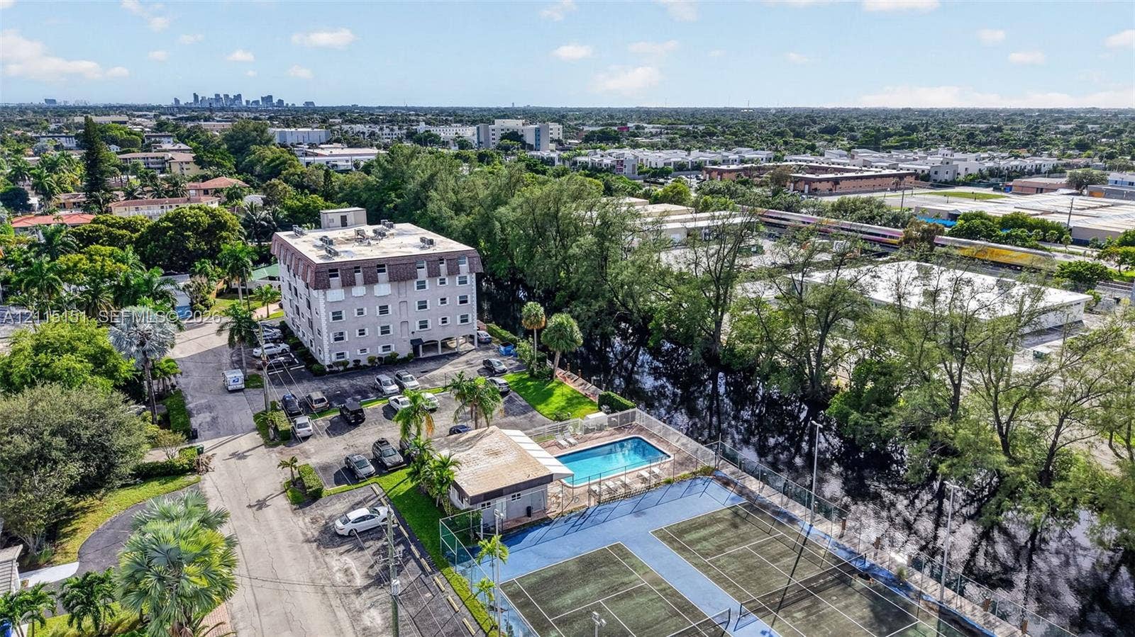 5951 NE 14th Lane, #408N, Fort Lauderdale, FL 33334 Aerial perspective of the residential complex featuring a swimming pool, two tennis courts, surface parking, and extensive mature landscaping