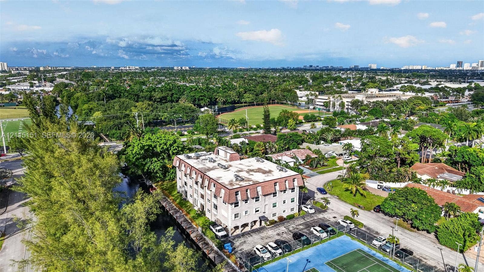 5951 NE 14th Lane, #408N, Fort Lauderdale, FL 33334 Aerial view of mid-rise multi-story building with a mansard roof, paved surface parking, and on-site tennis courts