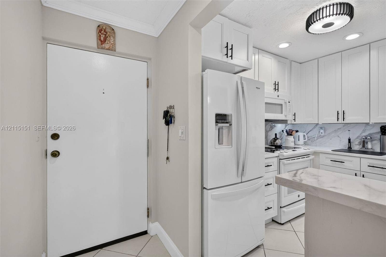 5951 NE 14th Lane, #408N, Fort Lauderdale, FL 33334 Kitchen featuring white shaker-style cabinetry, matte black hardware, stone-finish countertops, tile flooring, and integrated white appliances