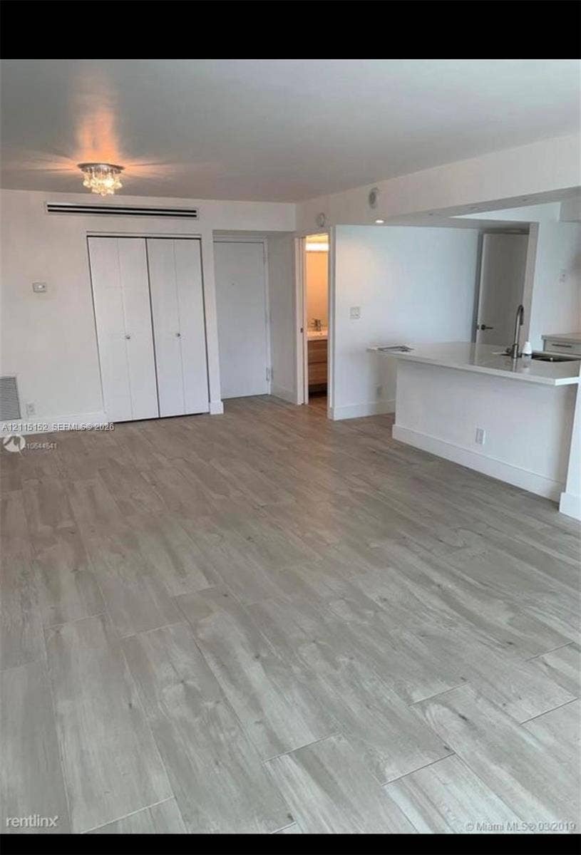 Interior space featuring wood-finish flooring, a kitchen breakfast bar with a stainless steel sink, recessed ceiling lighting, and built-in closet cabinetry