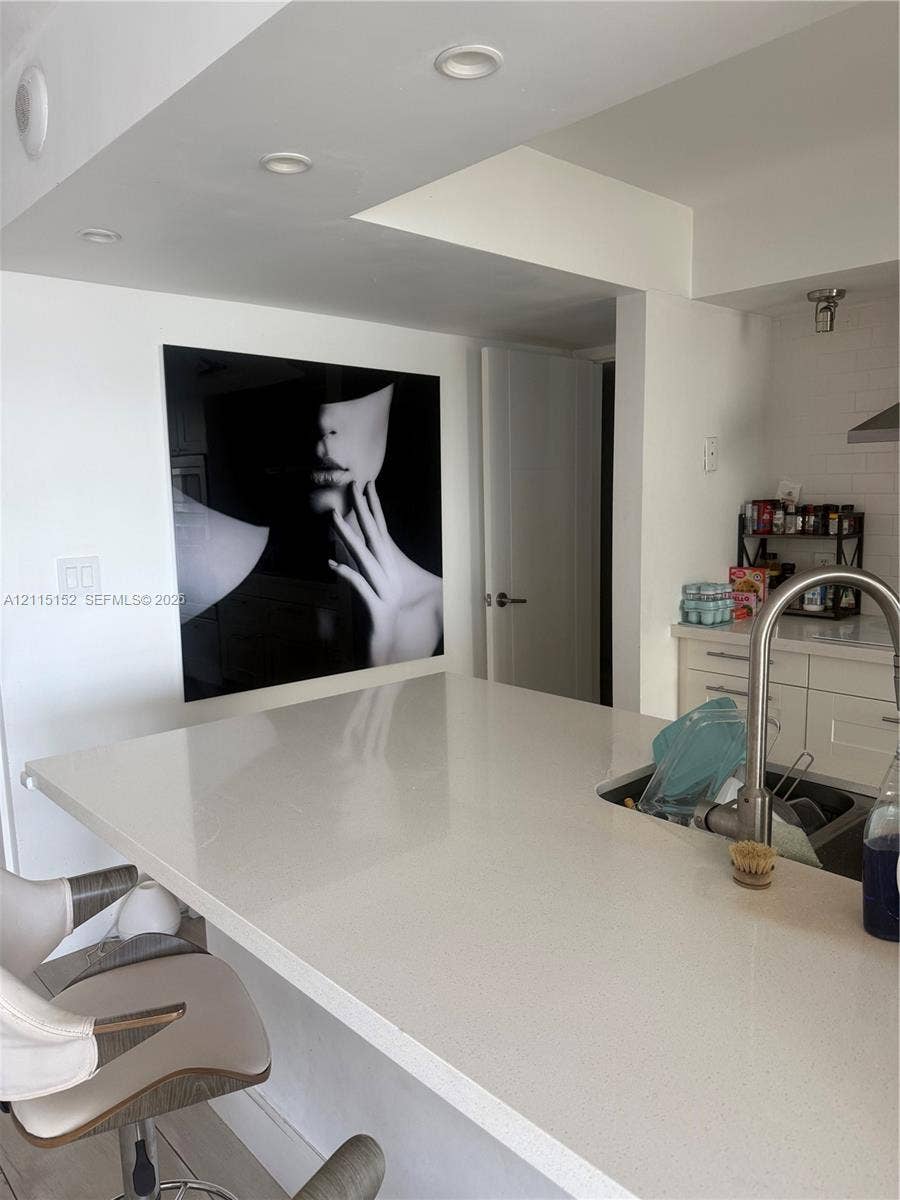 Kitchen featuring a quartz countertop island, undermount stainless steel sink, gooseneck faucet, white shaker-style cabinetry, and recessed ceiling lighting