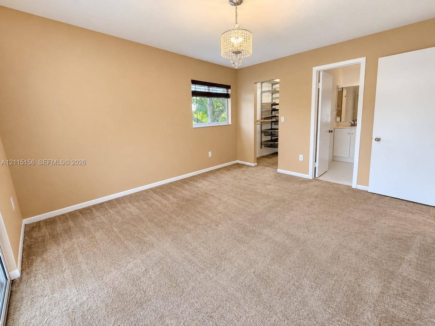 4800 NW 102nd Avenue, #201-10, Doral, Doral, FL 33178 Bedroom featuring neutral carpeting, a crystal-accented chandelier, a single-pane window, a walk-in storage area with built-in shelving, and a doorway to a separate tiled space