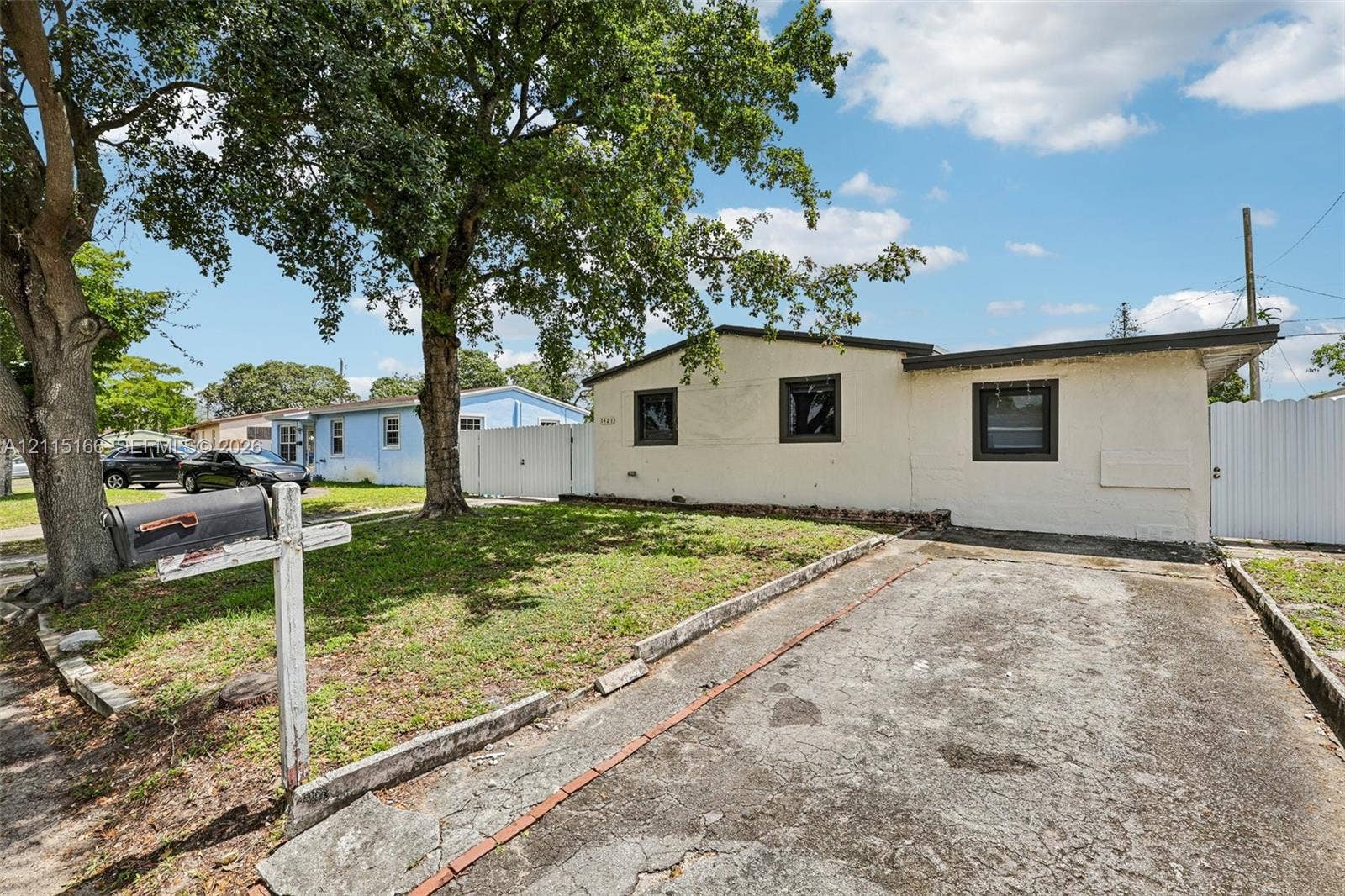 1421 N 68th Terrace, Hollywood, FL 33024 Single-story exterior featuring a concrete driveway, masonry walls, dark-framed windows, and a mature tree canopy