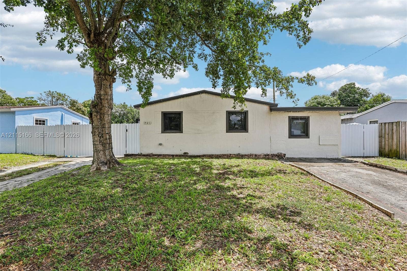 1421 N 68th Terrace, Hollywood, FL 33024 Single-story exterior with light-colored masonry, dark-framed windows, paved driveway, and white perimeter fencing