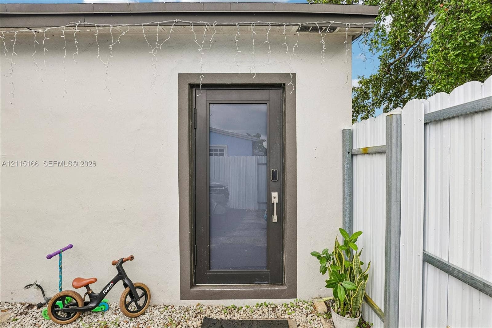 1421 N 68th Terrace, Hollywood, FL 33024 Exterior access point featuring a smooth stucco finish, a full-lite glass door with a dark frame, and white corrugated metal fencing