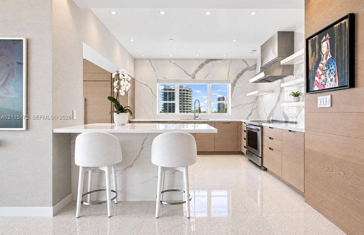 16 Island Avenue, #5C, Miami Beach, FL 33139 Kitchen featuring a waterfall-edge stone island, veined stone backsplash, stainless steel range hood, flat-panel wood-finish cabinetry, and recessed ceiling lighting