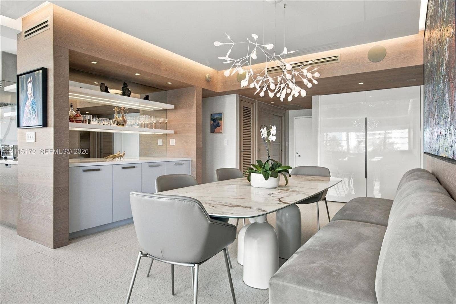 16 Island Avenue, #5C, Miami Beach, FL 33139 Custom built-in cabinetry with integrated lighting and stone surfacing, complemented by light-toned wood-finish wall paneling, high-gloss cabinetry, and a modern sculptural chandelier
