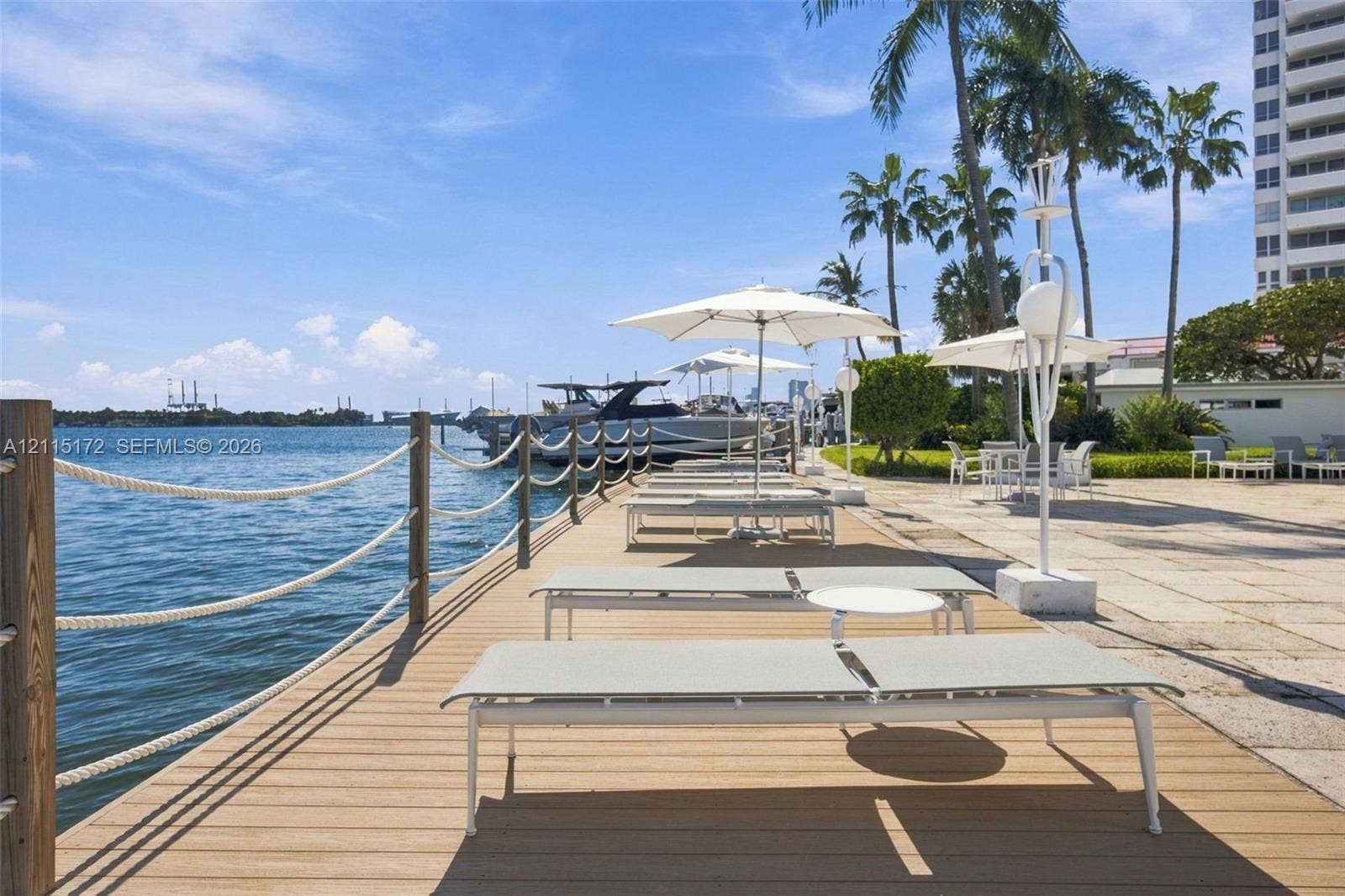16 Island Avenue, #5C, Miami Beach, FL 33139 Waterfront deck featuring wood-finish decking, rope railing, stone-paved patio area, and mature palm trees