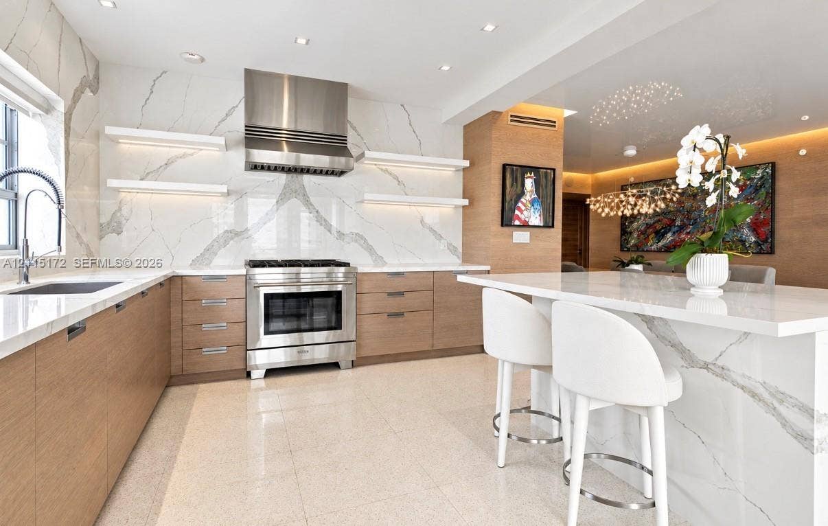 16 Island Avenue, #5C, Miami Beach, FL 33139 Kitchen featuring flat-panel wood cabinetry, a waterfall-edge island, a floor-to-ceiling stone-slab backsplash, integrated stainless steel range, and floating display shelving