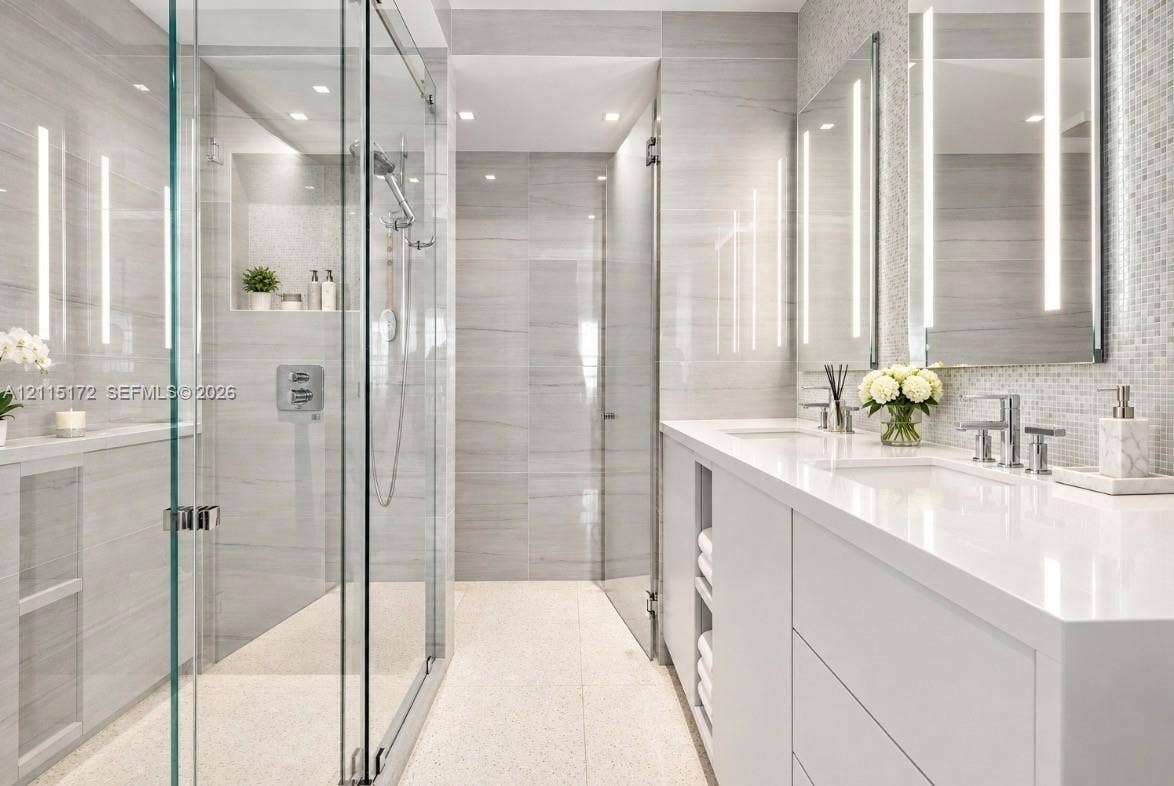 16 Island Avenue, #5C, Miami Beach, FL 33139 Walk-in glass-enclosed shower featuring large-format tile wall cladding, integrated wall niche, dual-sink vanity with white stone countertop, and vertical LED-lit vanity mirrors