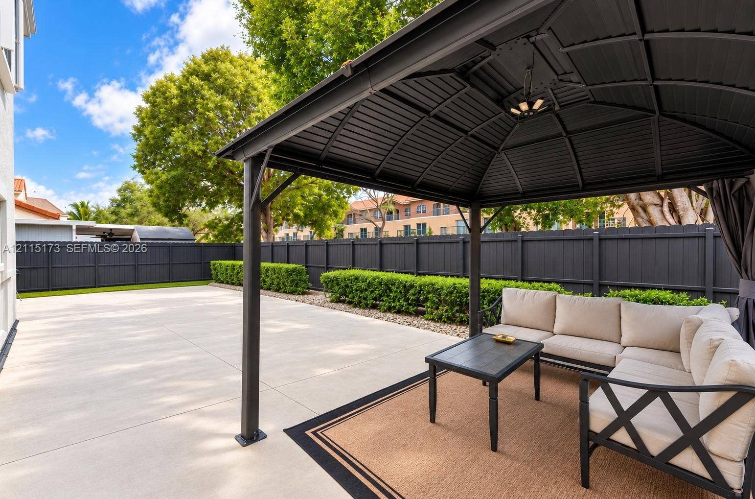 Hardscaped concrete patio featuring a metal gazebo, privacy fencing, and manicured shrubbery