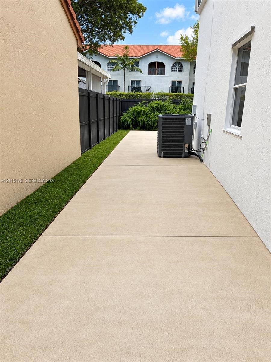 Side yard featuring a concrete walkway, synthetic turf border, and a perimeter privacy fence