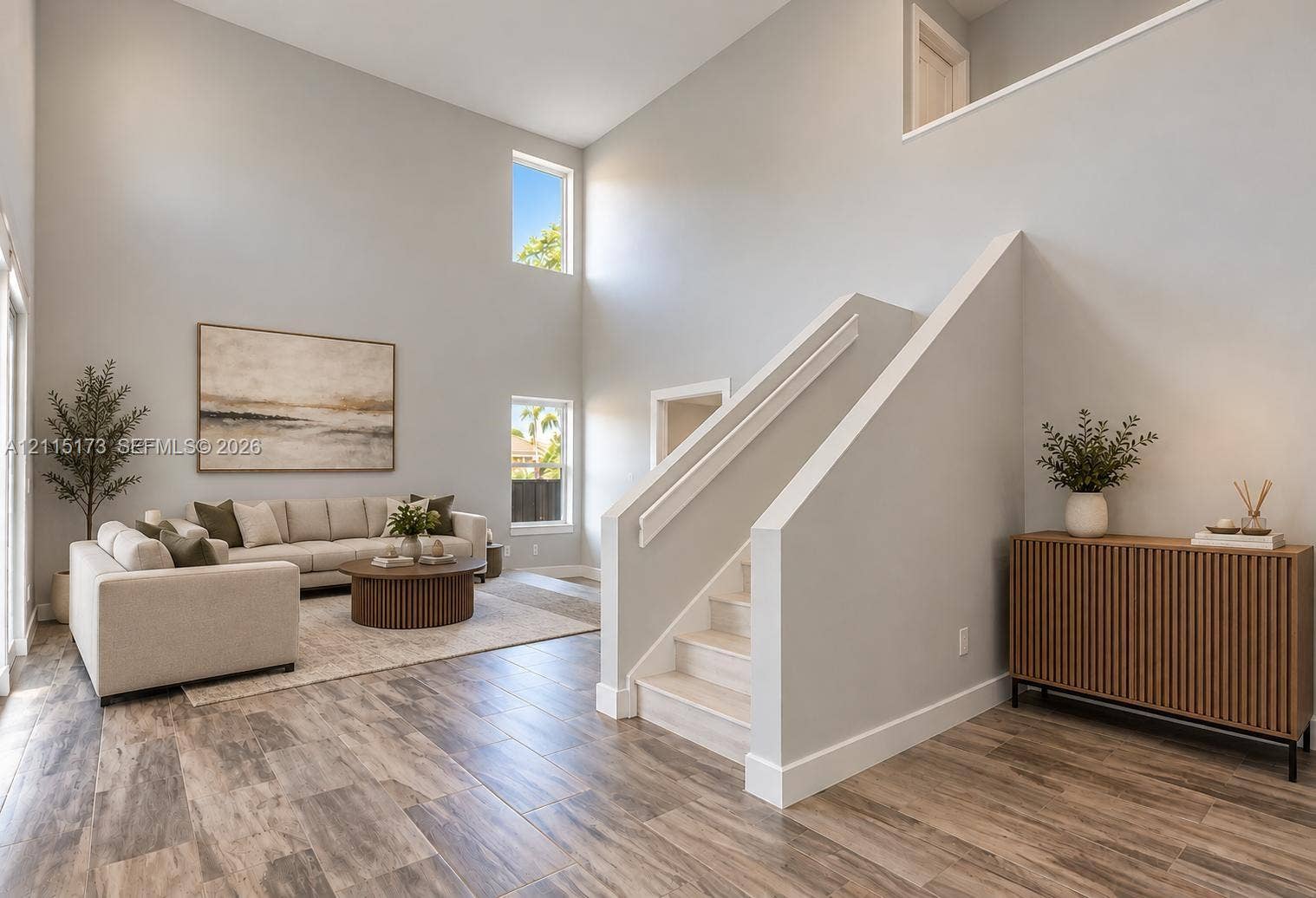 High-ceiling interior featuring wood-finish flooring, staircase with a solid-panel railing, and multiple vertical windows