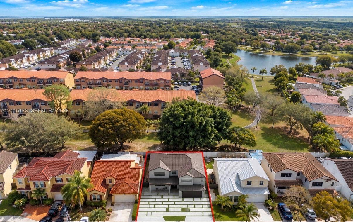 Aerial perspective of a multi-story residence featuring a tile roof, a multi-car garage, and a paved driveway with integrated turf grid patterns