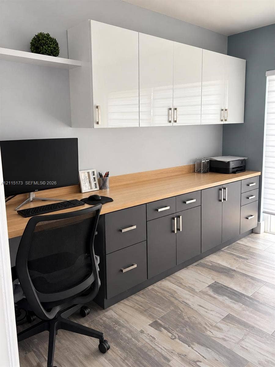 Built-in cabinetry featuring white gloss upper cupboards, charcoal lower drawers and cabinets, wood-finish countertop, floating display shelf, and light-tone wood-finish flooring