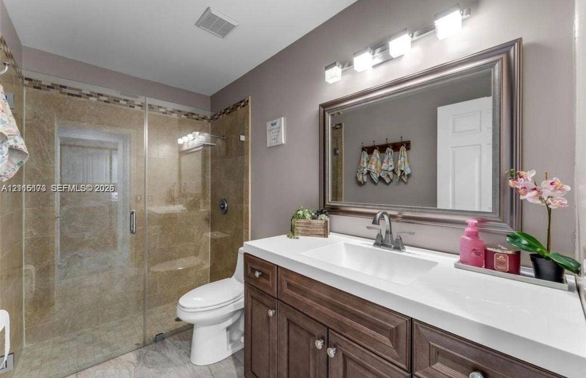 Bathroom featuring a vanity with a white countertop and rectangular undermount sink, a framed mirror, a four-light fixture, and a glass-enclosed shower with tile surround
