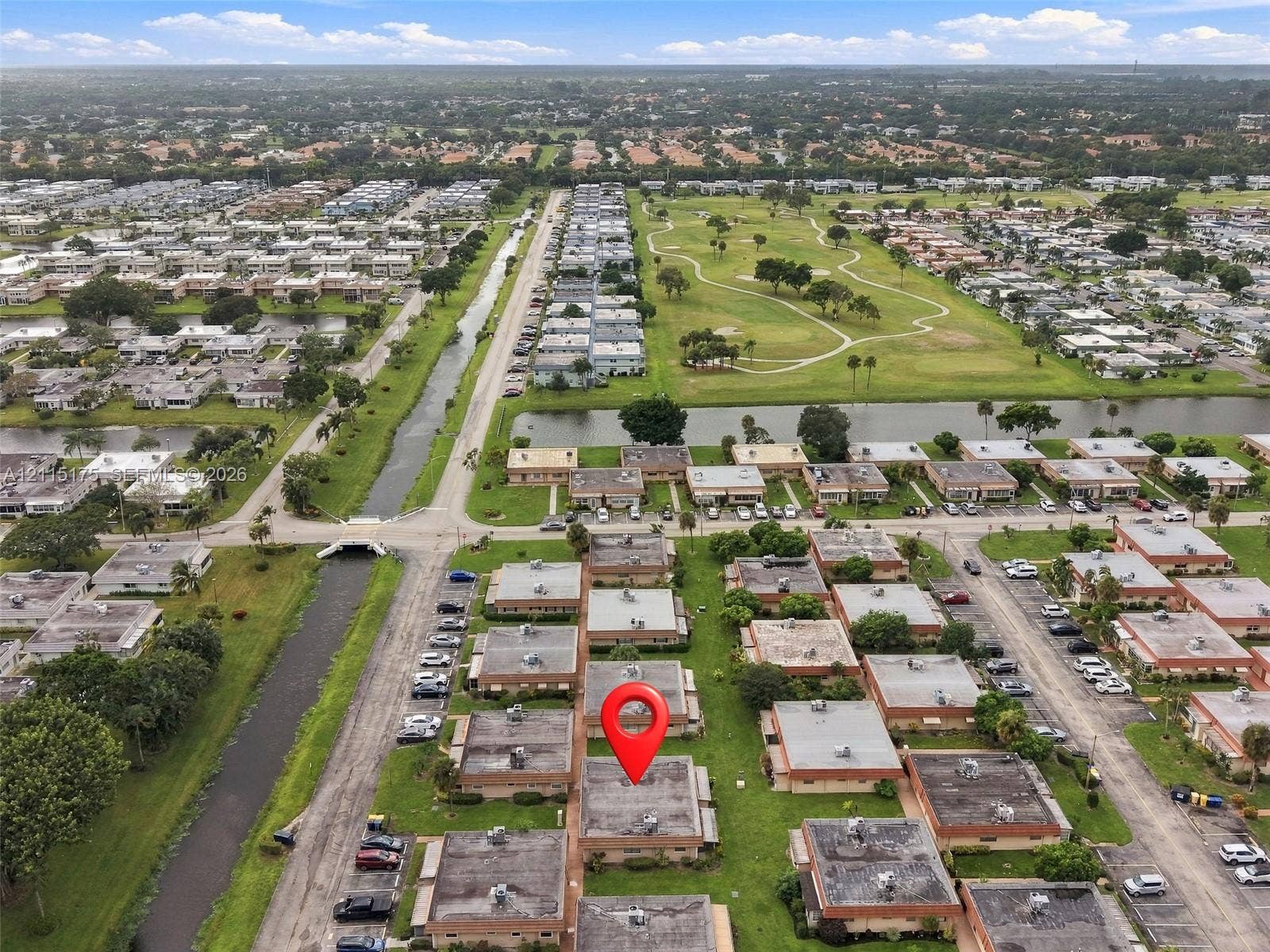 324 Seville N, Delray Beach, FL 33446 Aerial perspective of a multi-unit residential complex featuring manicured green spaces, water frontage, and proximity to a golf course with a red pin on this listing