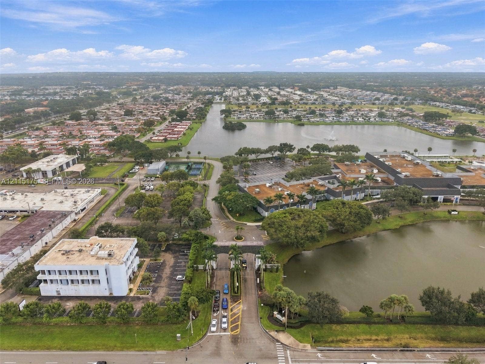 324 Seville N, Delray Beach, FL 33446 Aerial perspective showing one of the main entrances featuring gated access, expansive water frontage, mature trees, and the main clubhouse on the righ
