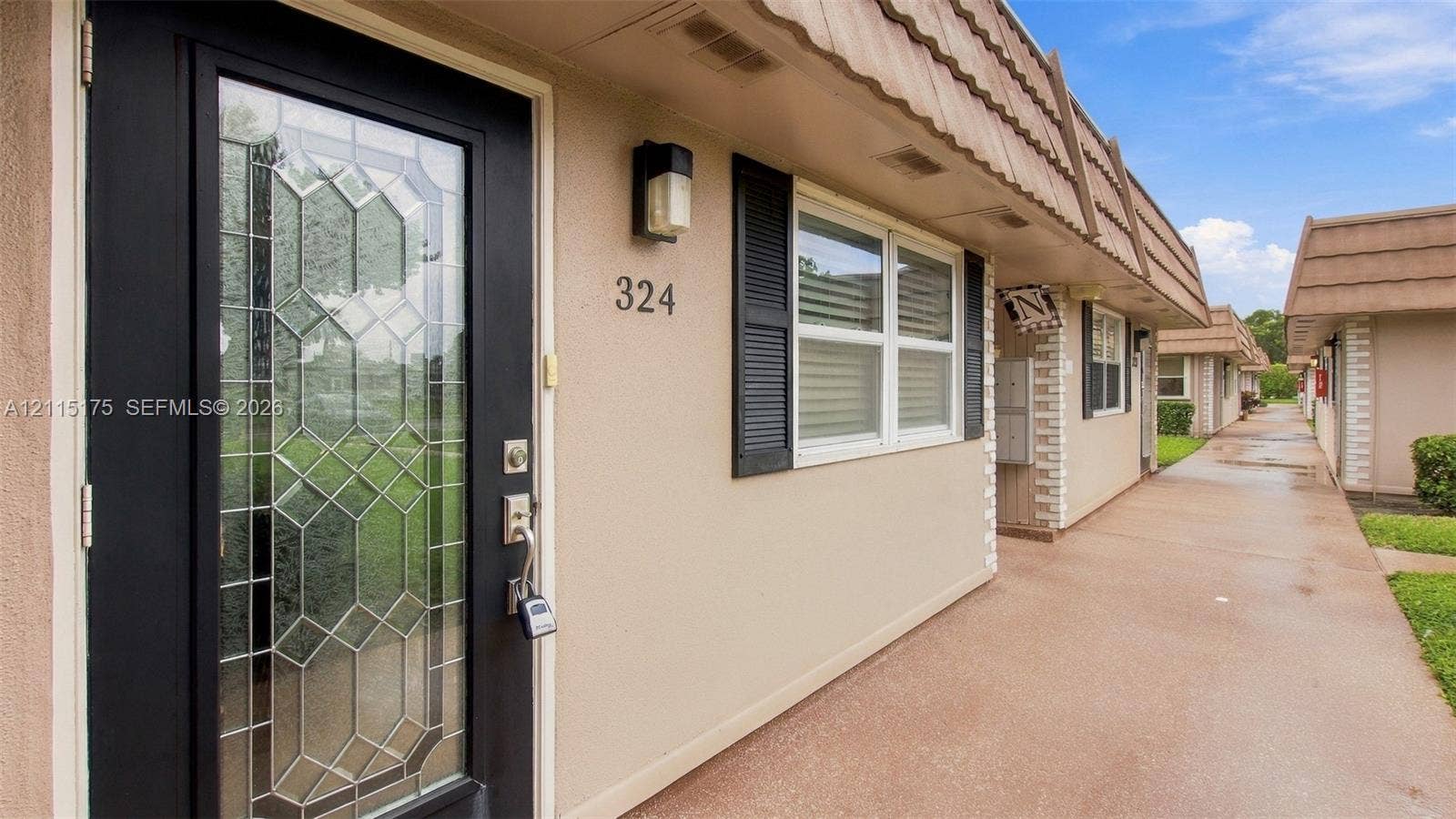 324 Seville N, Delray Beach, FL 33446 Exterior entry featuring a glass-panel door with decorative leaded accents, dark-framed window shutters, and a concrete walkway