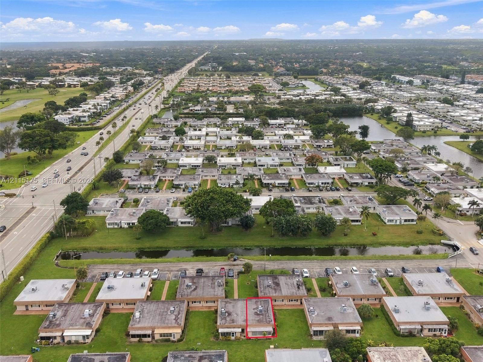 324 Seville N, Delray Beach, FL 33446 Aerial perspective of a single-story residence featuring a flat roofline, integrated exterior HVAC units, and direct access to a paved parking area, situated within a landscaped neighborhood with water features