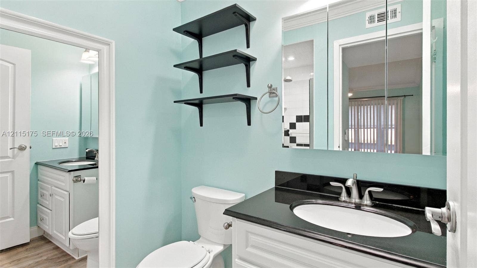 324 Seville N, Delray Beach, FL 33446 Primary bathroom featuring white cabinetry, a dark stone countertop, an integrated oval sink, and a large mirrored medicine cabinet, complemented by matte black wall-mounted shelving